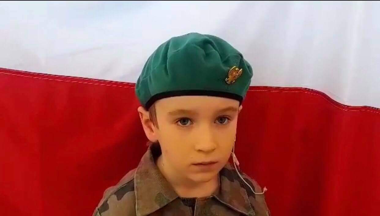 Zdjęcie dziecka w stroju żołnierza na tle flagi RP